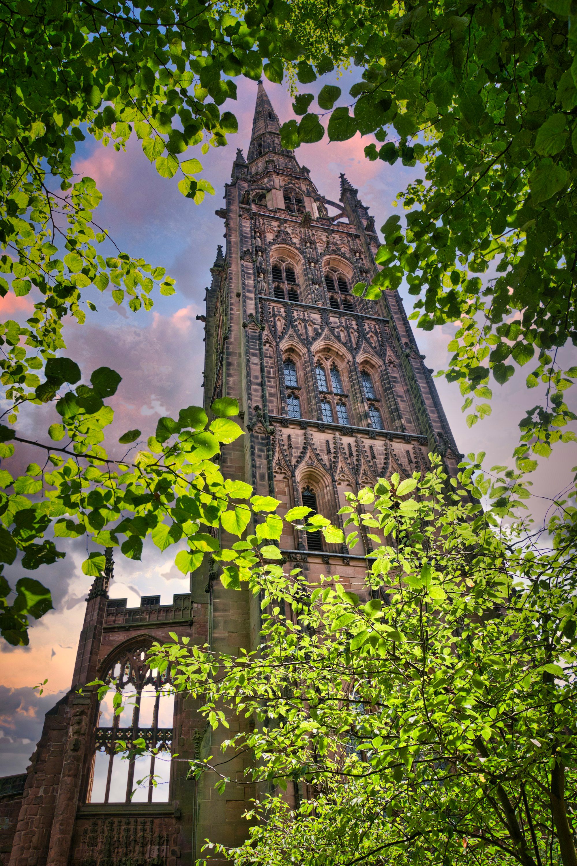 A Coventry church tower framed by green leaves