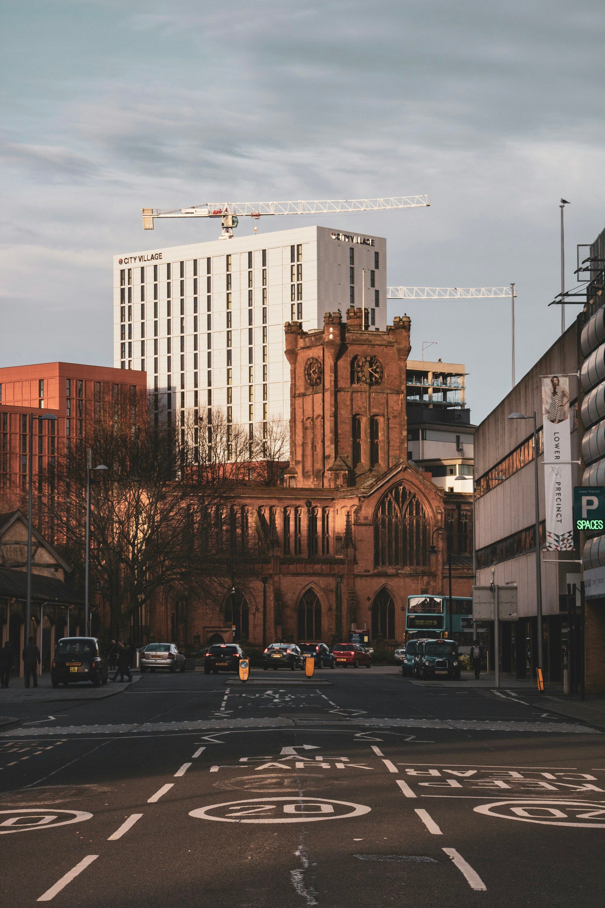 A Coventry church tower beside modern city-centre buildings